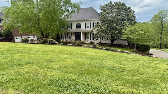 colonial house featuring covered porch, an attached garage, and a front lawn