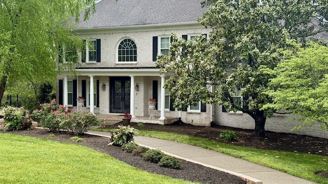 view of front facade with roof with shingles, a porch, a front lawn, and brick siding