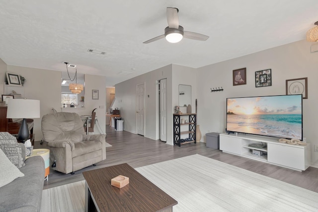 living room with baseboards, ceiling fan, visible vents, and wood finished floors