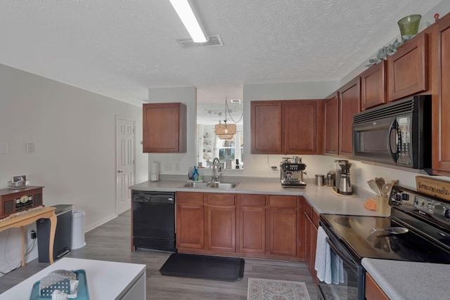 kitchen with a sink, light countertops, wood finished floors, visible vents, and black appliances