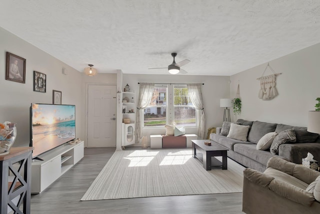 living area with a ceiling fan, a textured ceiling, and wood finished floors