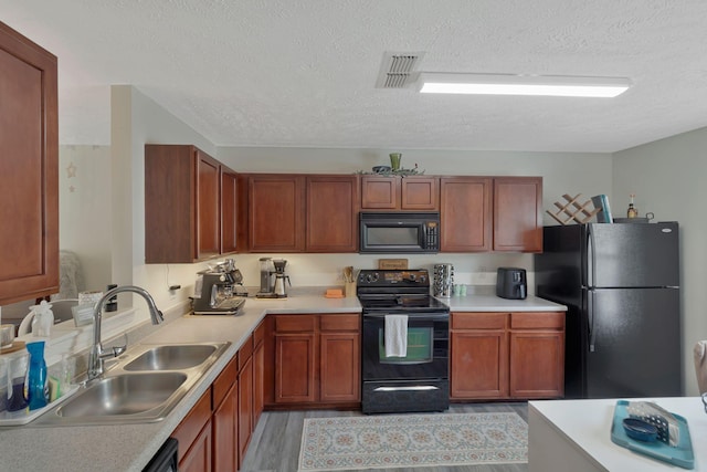 kitchen with a sink, light countertops, a textured ceiling, visible vents, and black appliances