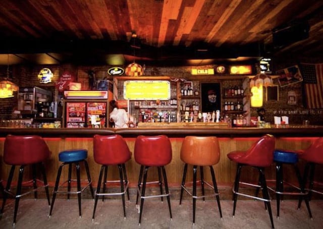 bar with a dry bar, wood ceiling, and unfinished concrete flooring