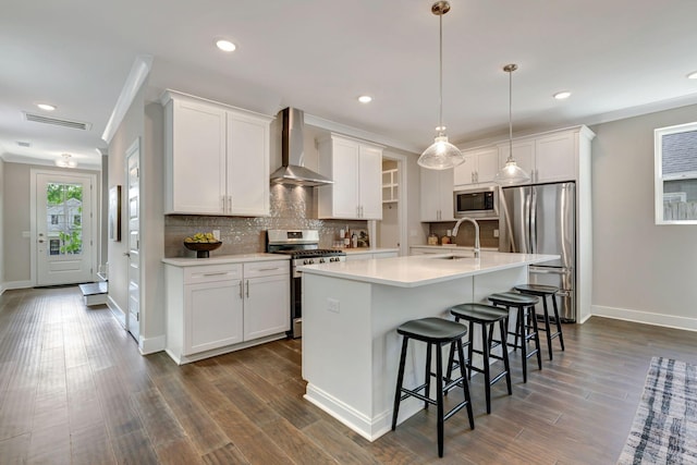 kitchen featuring baseboards, wall chimney exhaust hood, white cabinetry, appliances with stainless steel finishes, and backsplash
