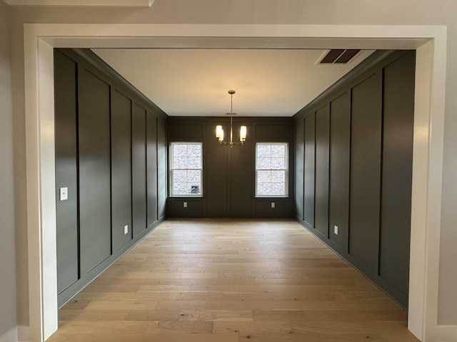 unfurnished dining area with visible vents, a decorative wall, light wood-style flooring, and a chandelier