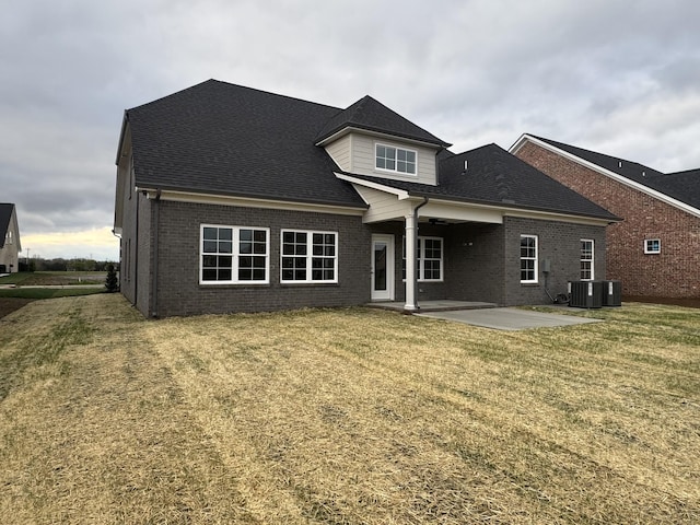 back of property featuring a shingled roof, central AC, brick siding, a patio area, and a lawn