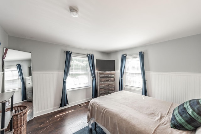 bedroom with multiple windows, wainscoting, dark wood-style floors, and visible vents