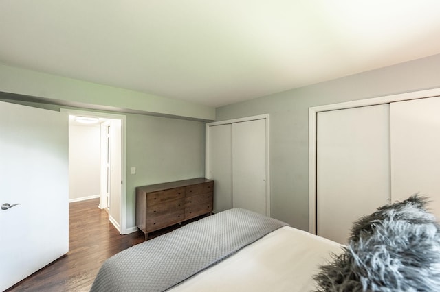 bedroom with baseboards, two closets, and dark wood finished floors
