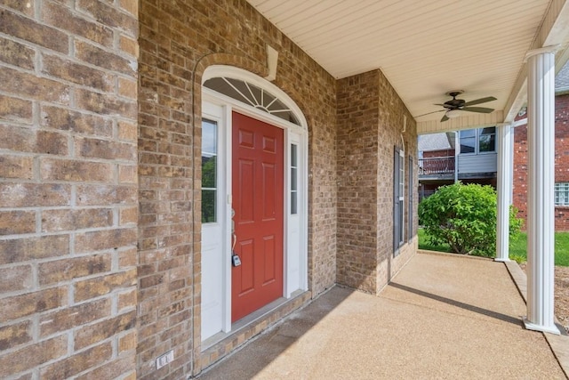 view of exterior entry with a ceiling fan, a porch, and brick siding