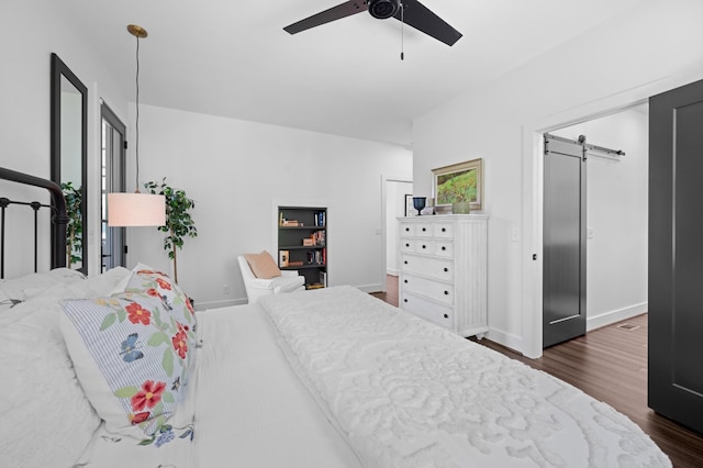 bedroom with baseboards, ceiling fan, a barn door, and dark wood-type flooring