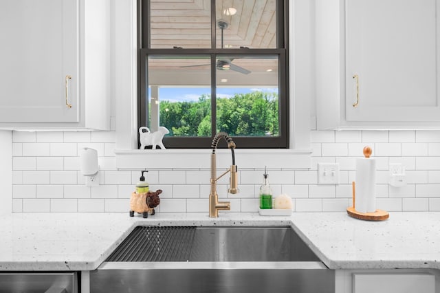 room details with a sink, decorative backsplash, light stone countertops, and white cabinets