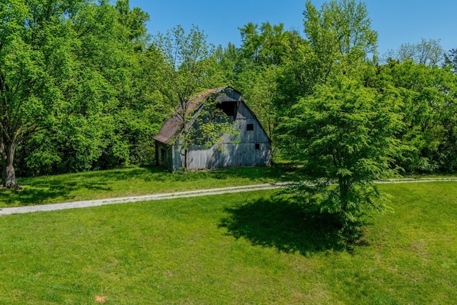 view of yard featuring a view of trees, a barn, and an outbuilding