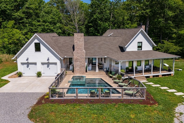 rear view of property featuring a chimney, a shingled roof, a lawn, a pool with connected hot tub, and driveway