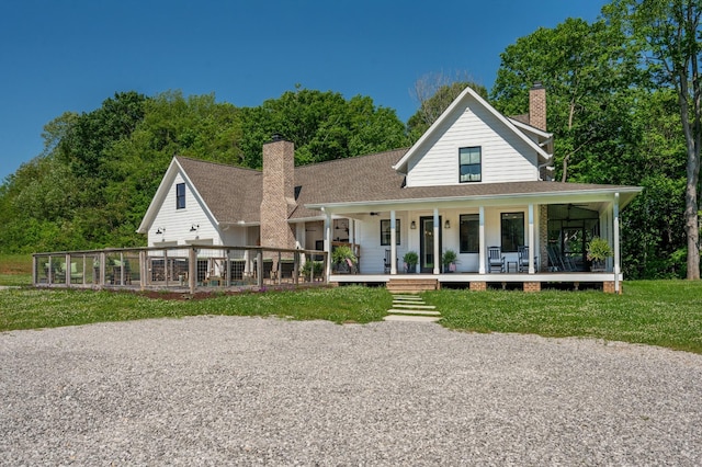 rear view of house with roof with shingles, covered porch, a chimney, and a yard