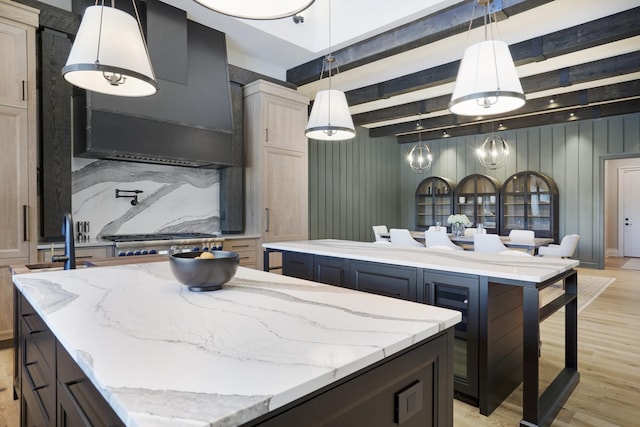 kitchen featuring light stone countertops, hanging light fixtures, light wood-style flooring, a kitchen island, and beamed ceiling