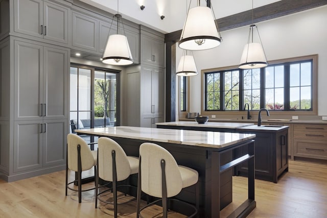kitchen with hanging light fixtures, a center island with sink, a sink, light stone counters, and light wood-style floors