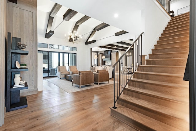 staircase featuring an inviting chandelier, lofted ceiling with beams, and wood finished floors