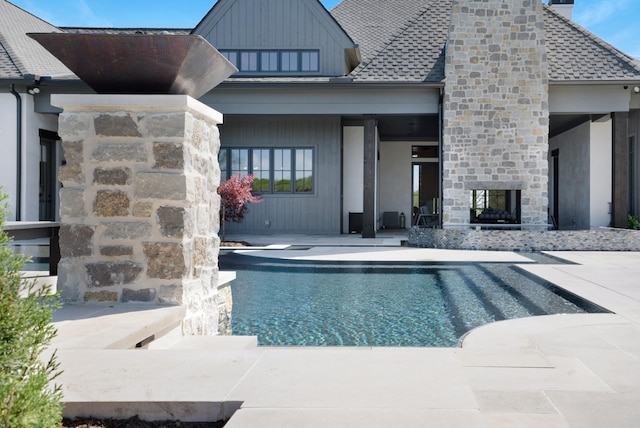 rear view of house with a multi sided fireplace, an outdoor pool, a patio area, a shingled roof, and stone siding