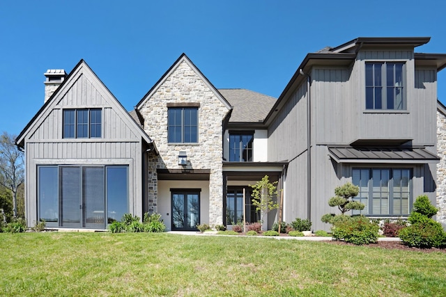 view of front of property with stone siding, a front yard, a chimney, a standing seam roof, and metal roof