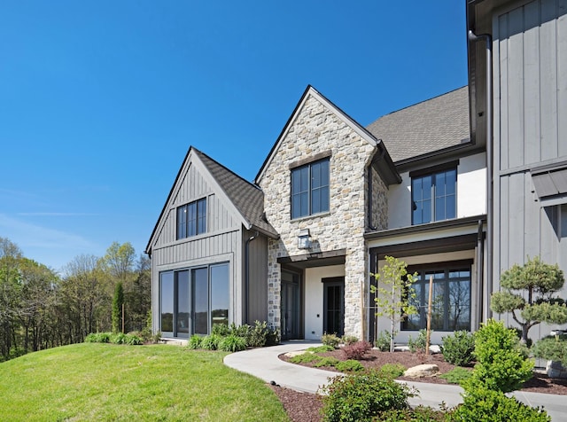 view of front of home featuring board and batten siding, roof with shingles, a front yard, and stone siding
