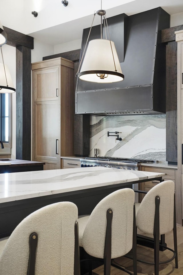kitchen with range hood, light stone counters, a sink, light wood finished floors, and hanging light fixtures