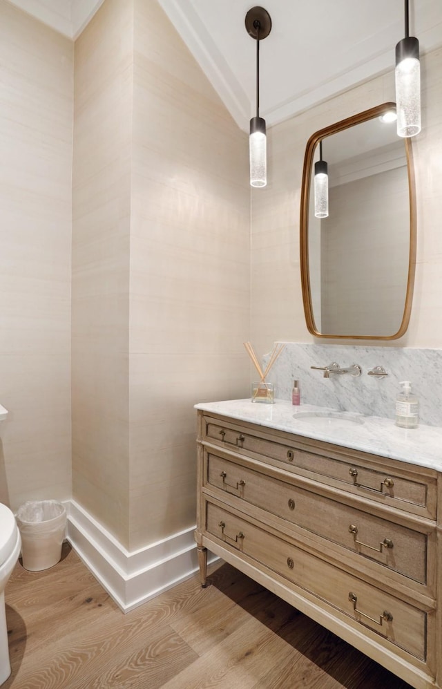 half bath featuring vanity, ornamental molding, wood finished floors, and toilet