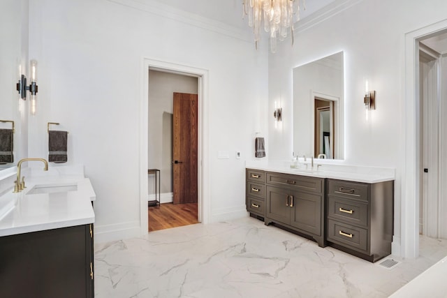bathroom with crown molding, a notable chandelier, a sink, marble finish floor, and two vanities