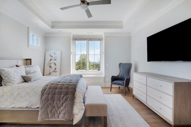 bedroom featuring crown molding, a ceiling fan, a tray ceiling, and light wood-style flooring