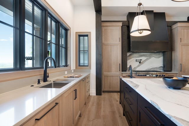 kitchen featuring pendant lighting, light brown cabinetry, light stone countertops, a sink, and light wood-style flooring