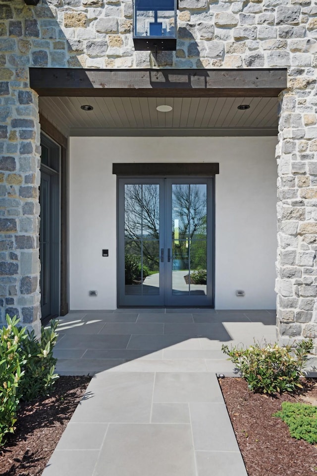 property entrance with stucco siding, french doors, and stone siding