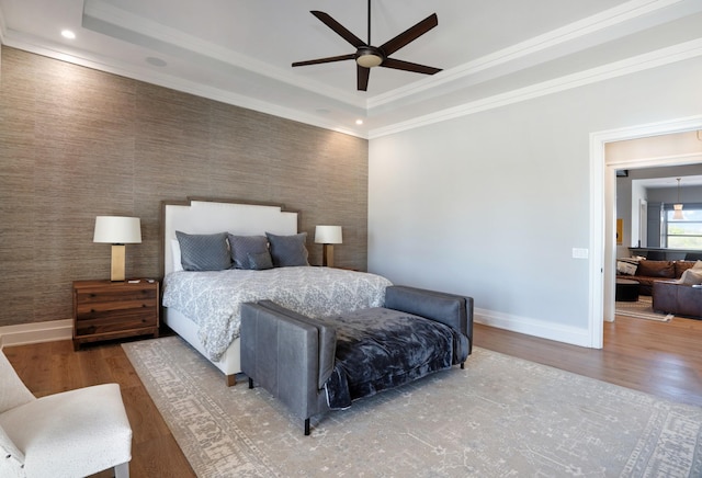 bedroom featuring baseboards, ornamental molding, a tray ceiling, and wood finished floors