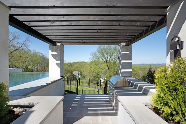 view of patio with fence, grilling area, a pergola, an outdoor kitchen, and a wooded view