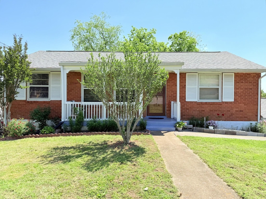 view of front facade with a shingled roof, a porch, a front lawn, and brick siding