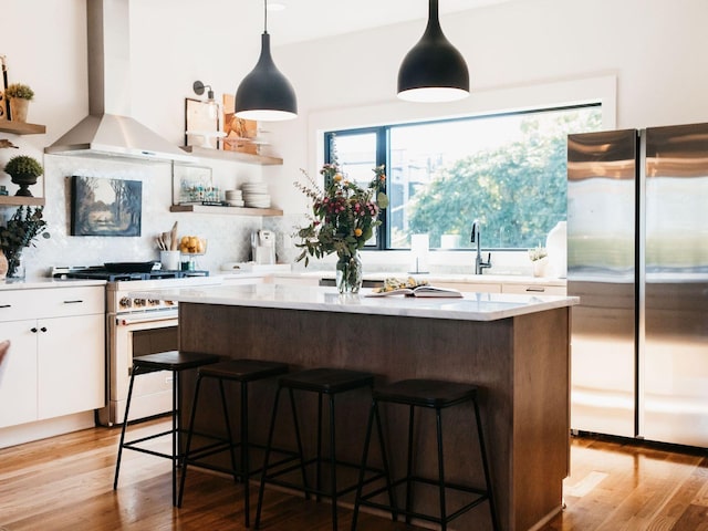 kitchen featuring wall chimney range hood, a center island, light countertops, white cabinets, and stainless steel appliances