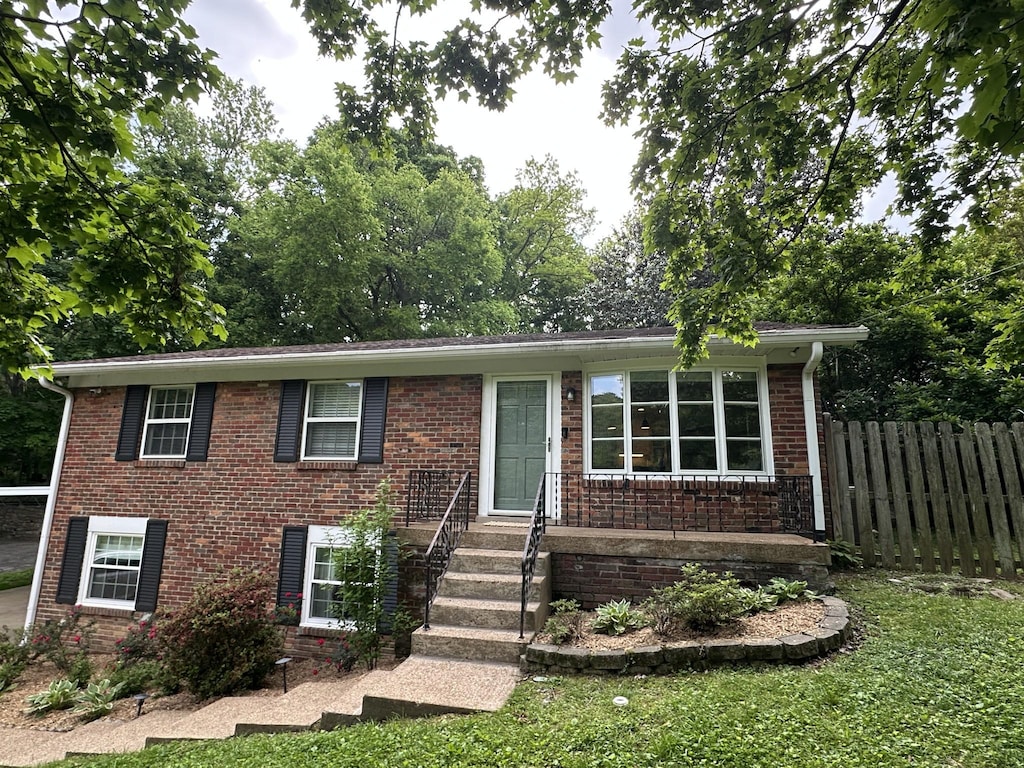 view of front of home featuring brick siding, fence, and a front lawn