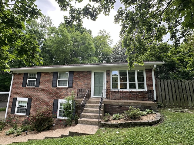 view of front of home featuring brick siding, fence, and a front lawn