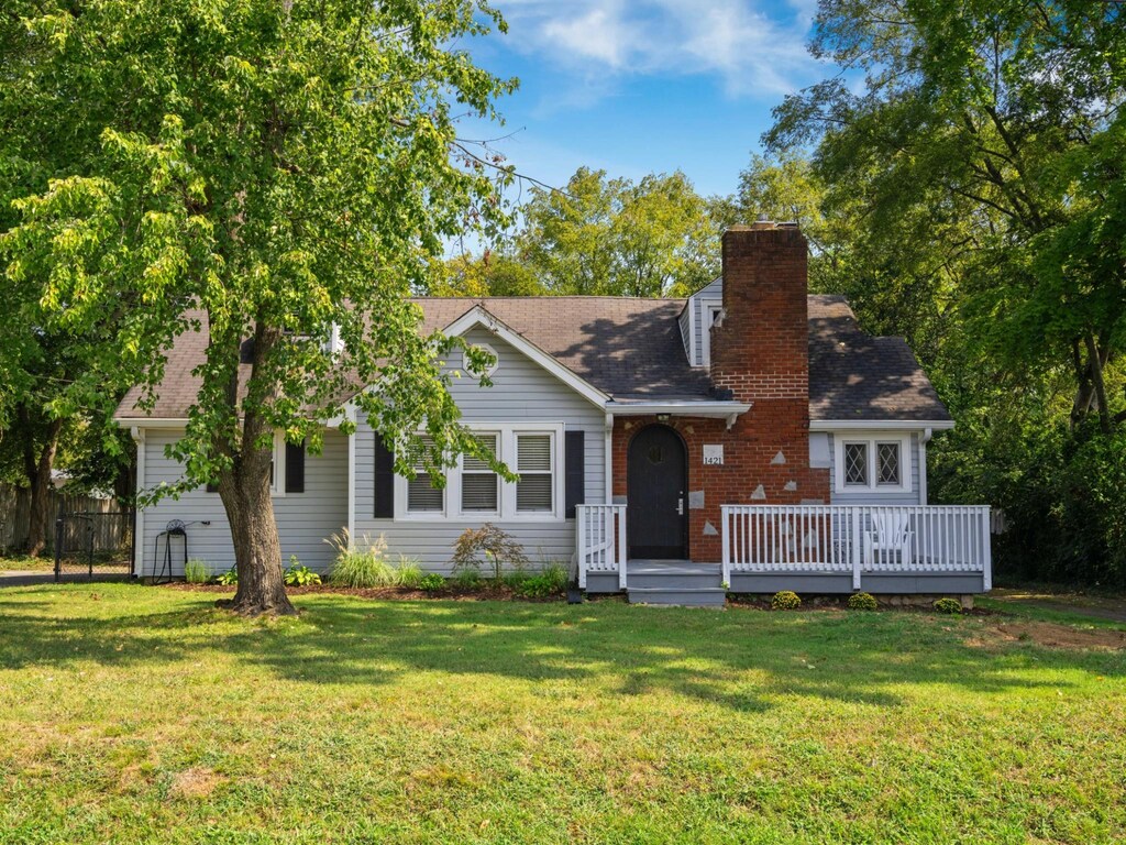 view of front of home with fence, roof with shingles, a front lawn, a wooden deck, and a chimney