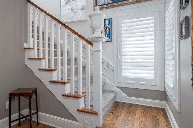 stairway with baseboards, wood finished floors, and a healthy amount of sunlight