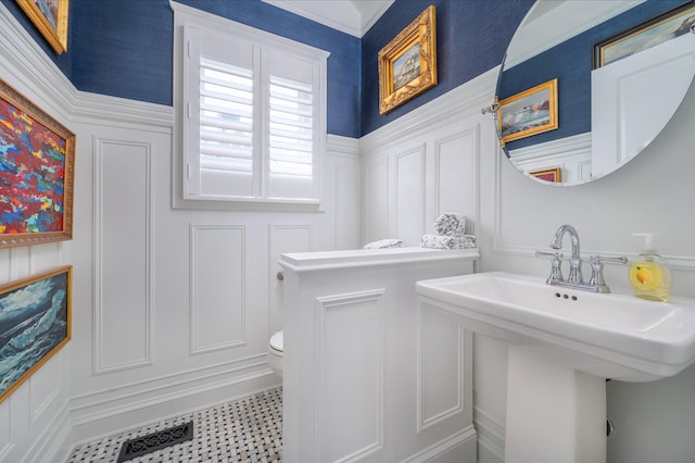 half bath featuring toilet, wainscoting, a sink, and a decorative wall