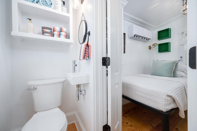 bathroom with toilet, baseboards, a wall unit AC, and wood finished floors