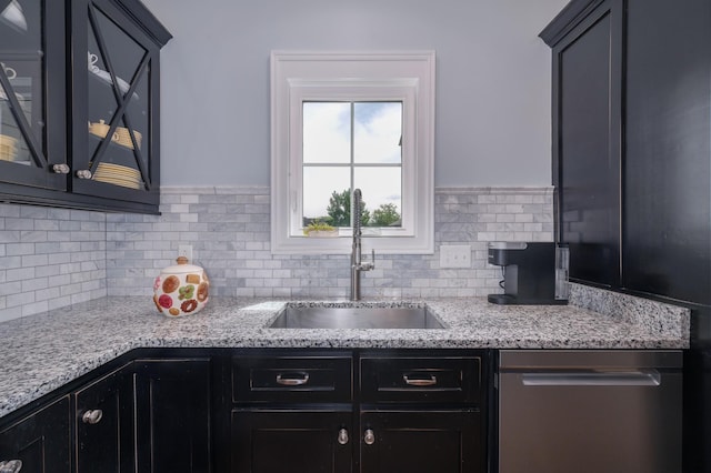 kitchen featuring stainless steel dishwasher, decorative backsplash, glass insert cabinets, dark cabinets, and a sink