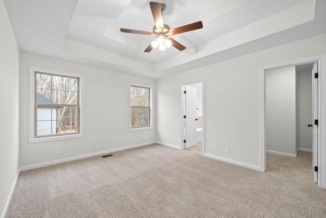 empty room with a tray ceiling, light carpet, baseboards, and plenty of natural light