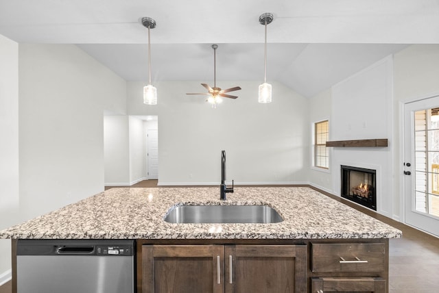 kitchen featuring dark brown cabinetry, stainless steel dishwasher, a sink, a warm lit fireplace, and open floor plan
