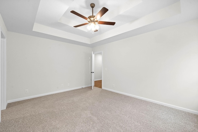 spare room with a tray ceiling, ceiling fan, light carpet, and baseboards
