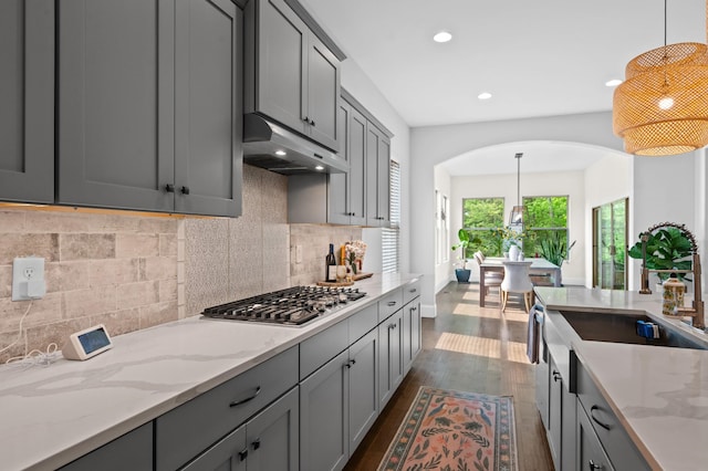 kitchen with gray cabinets, arched walkways, stainless steel gas cooktop, dark wood-style floors, and under cabinet range hood