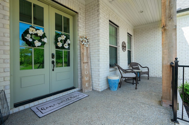 property entrance featuring french doors, a porch, and brick siding