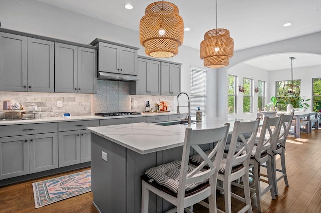 kitchen featuring arched walkways, gray cabinetry, a sink, and tasteful backsplash