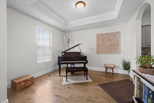 living area featuring crown molding, arched walkways, wood finished floors, and a raised ceiling