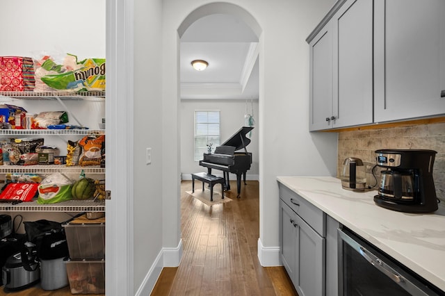 bar with backsplash, crown molding, arched walkways, a raised ceiling, and hardwood / wood-style floors