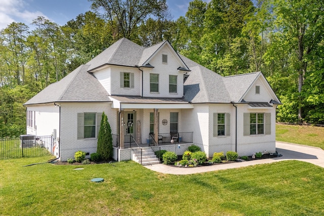 modern inspired farmhouse with covered porch, brick siding, fence, and a front lawn
